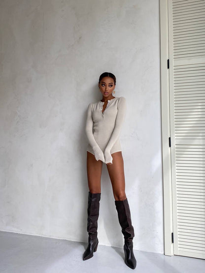 Person wearing a beige bodysuit and black knee-high boots against a plain wall.