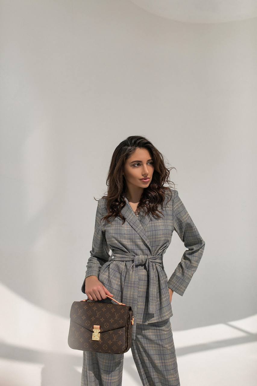 Woman in a gray checkered suit holding a brown bag against a white background