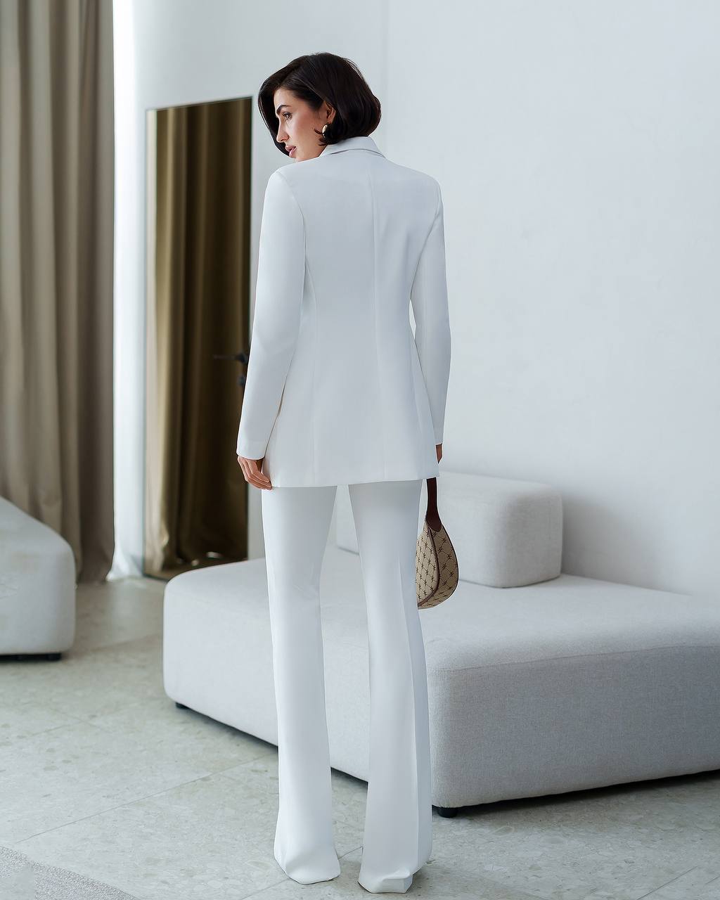 Woman in a white suit standing in a modern living room.