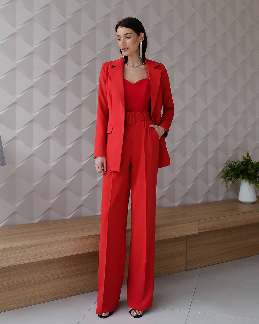 Woman in a red outfit standing against a geometric-patterned wall.
