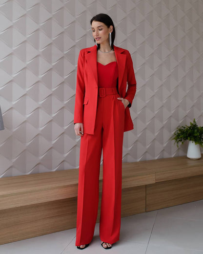 Woman in a red outfit standing against a geometric-patterned wall.