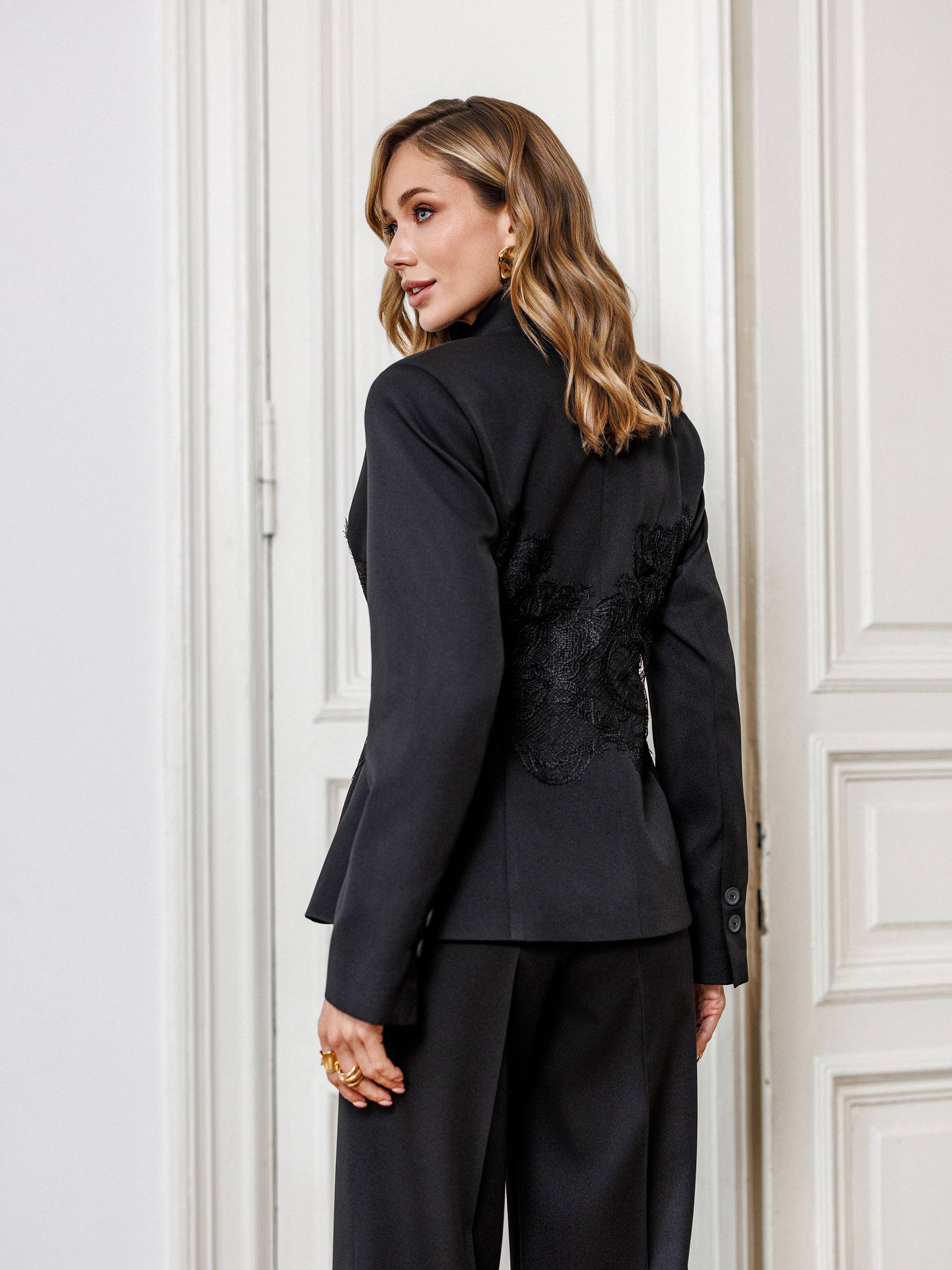 Woman wearing a black suit with decorative elements in a room with white paneled walls.