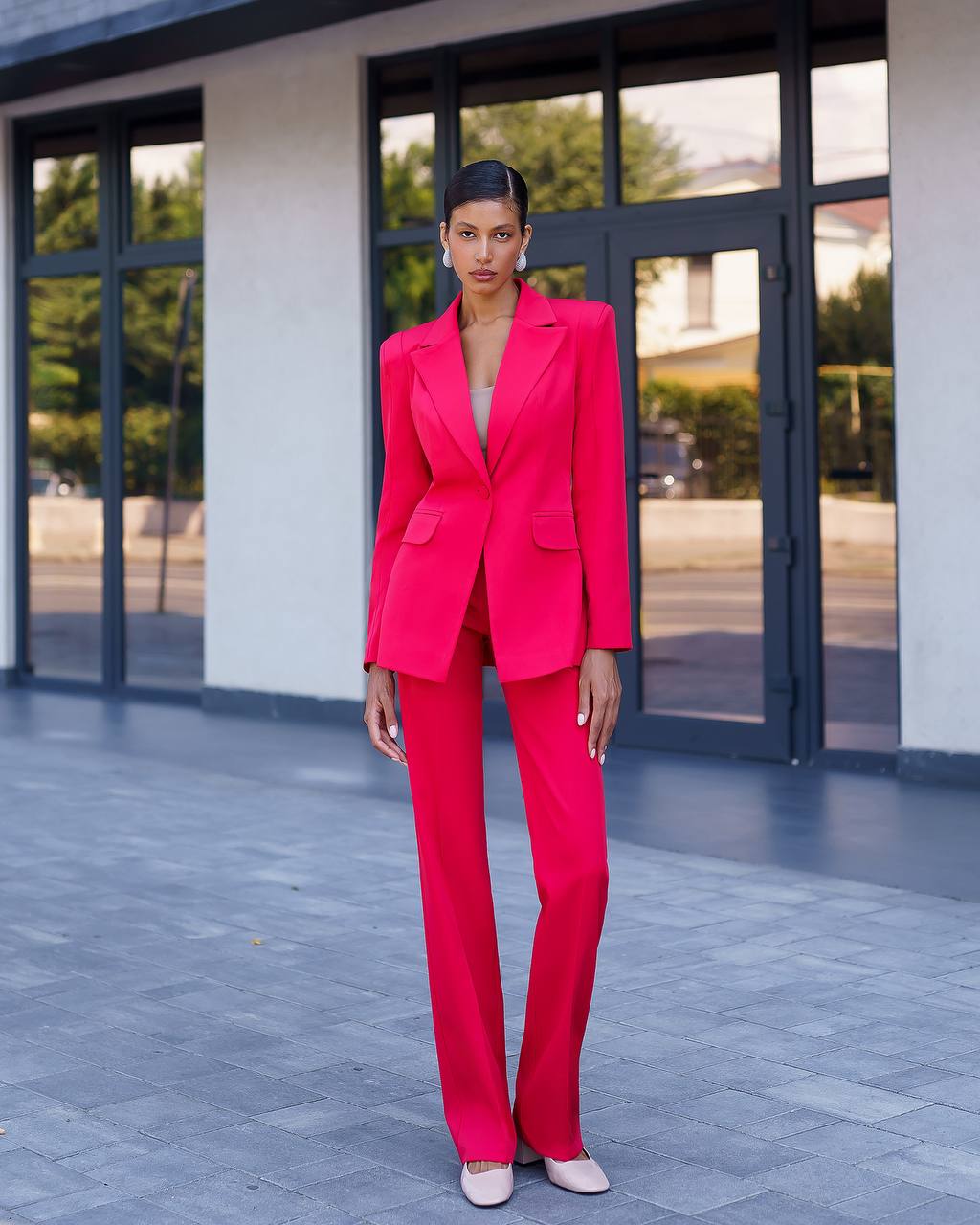 Woman in a bright pink suit standing in front of a building with large windows.