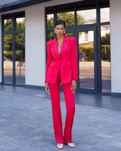 Woman in a bright pink suit standing in front of a building with large windows.