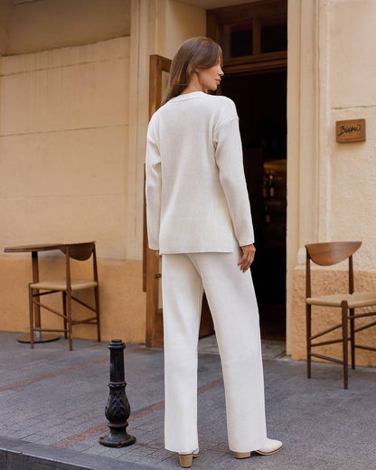 Woman in a white suit standing outside a building with chairs and a table in the foreground.