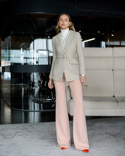 Woman in a checkered blazer and pink pants standing in an indoor setting.
