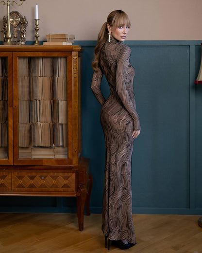 Woman in a textured dress standing in a room with wooden furniture and a blue wall.