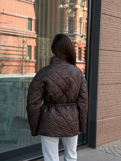 Person wearing a brown quilted jacket standing in front of a building entrance.