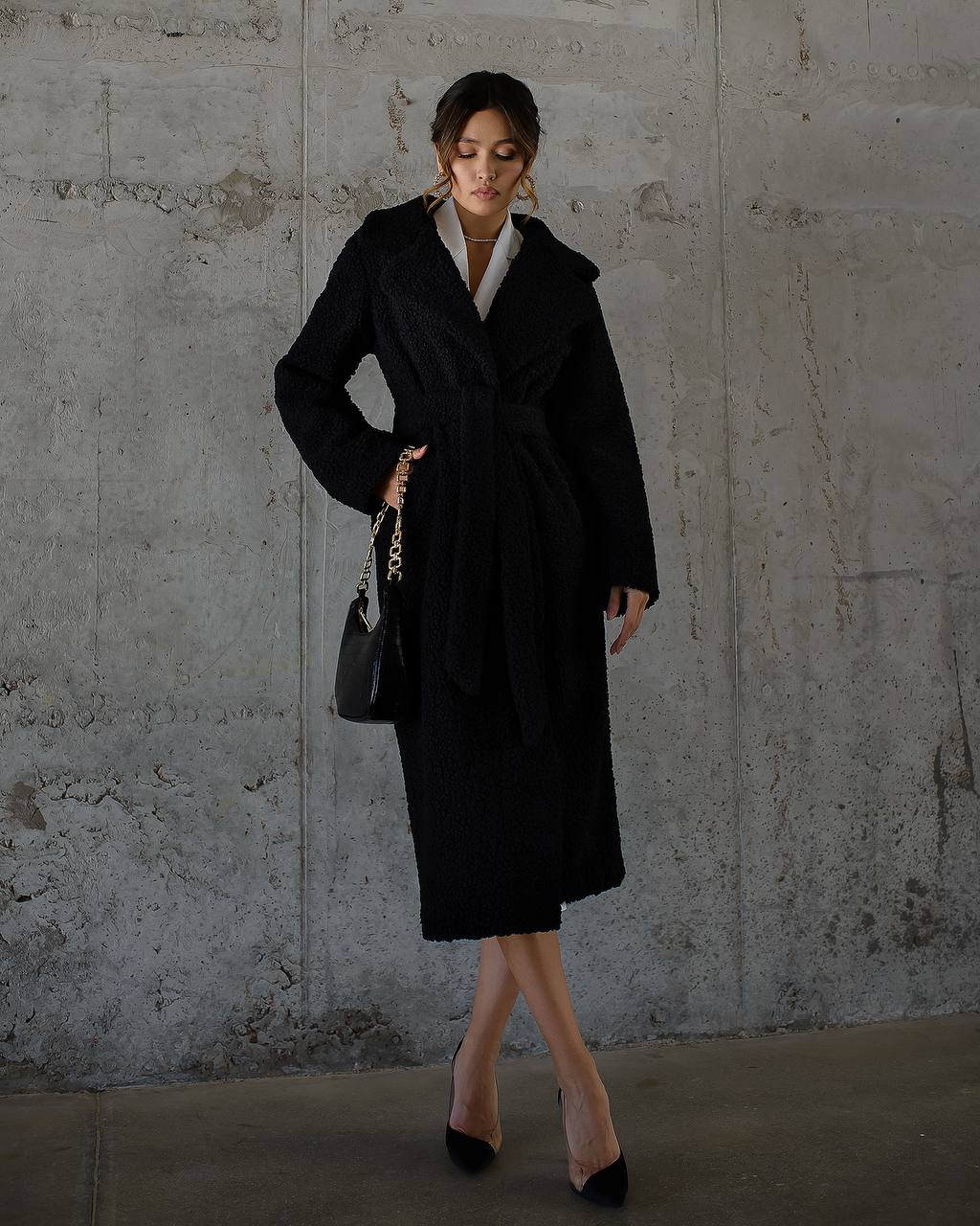 Woman wearing a black coat against a textured wall.