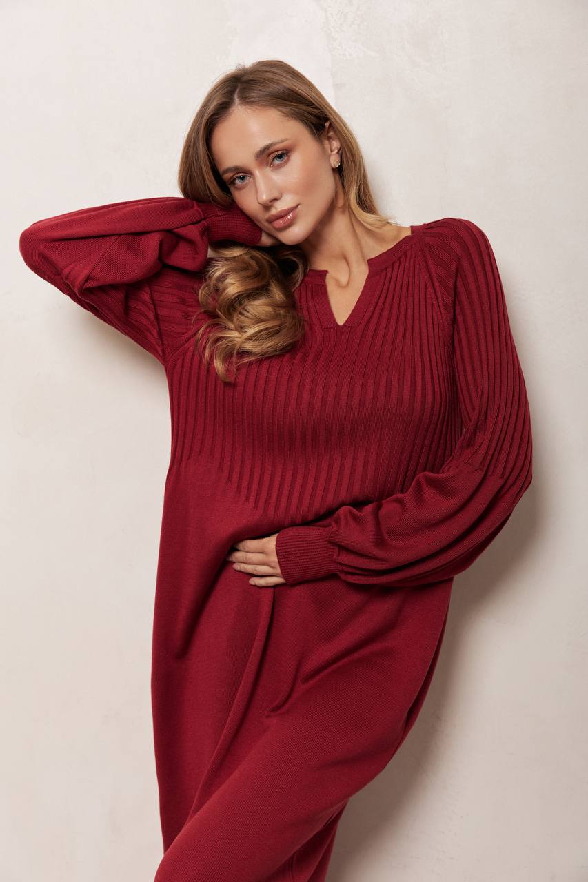 Woman wearing a red ribbed sweater and pants against a light background