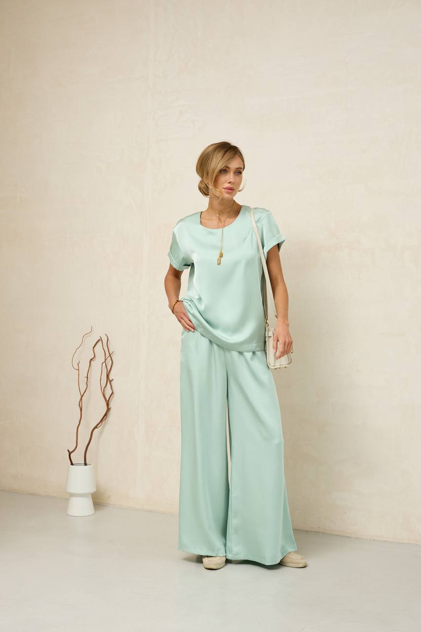 Woman wearing a light green outfit with wide-leg pants against a plain background