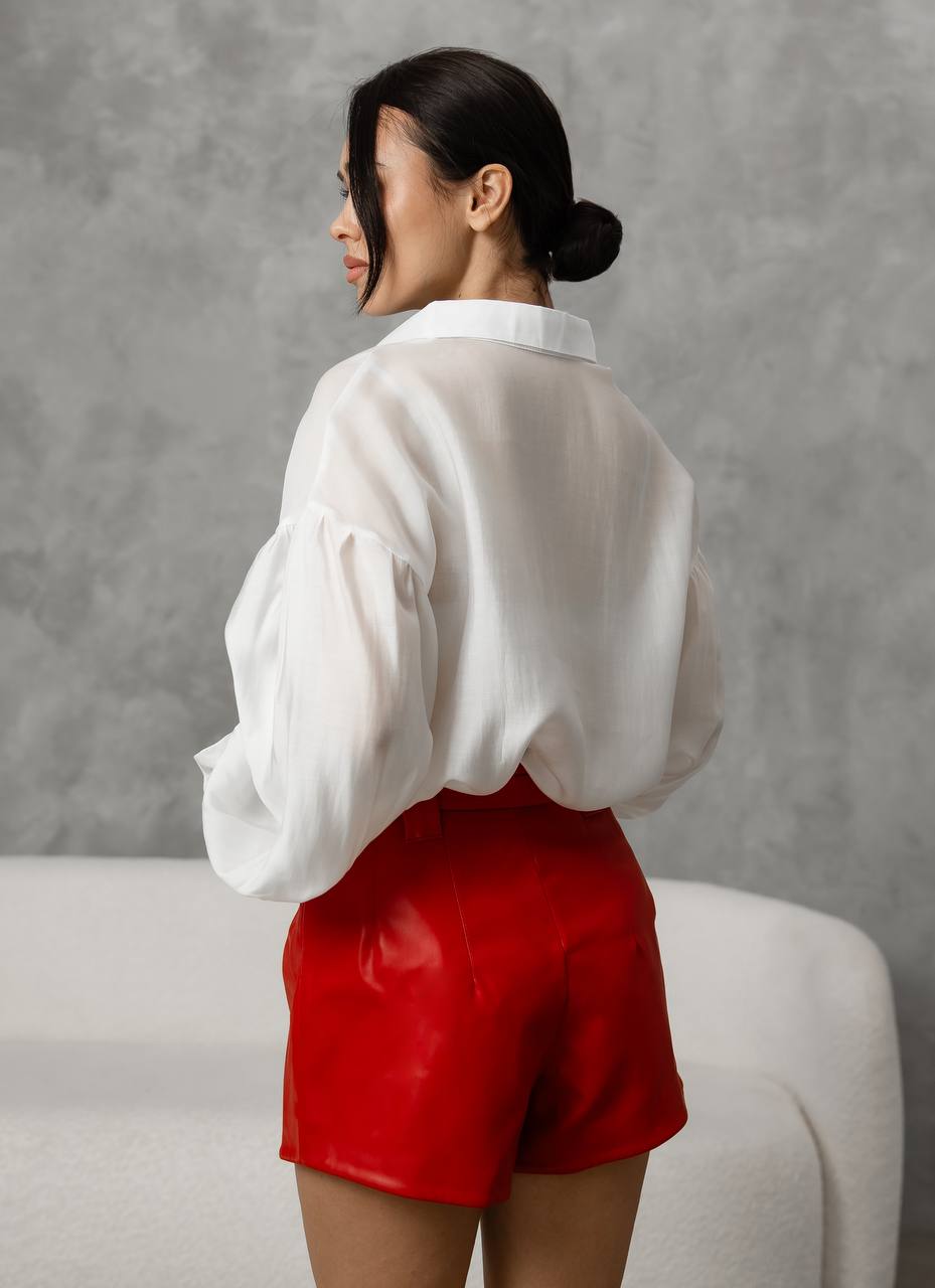 Woman wearing a white blouse and red shorts against a gray background