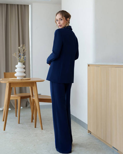 Woman in a navy blue suit standing in a modern room with wooden furniture and a light-colored wall.