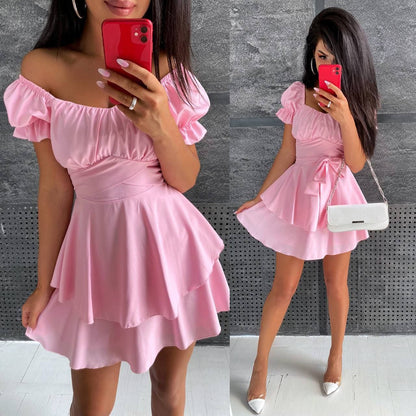 Woman wearing a pink off-shoulder dress against a gray wall.