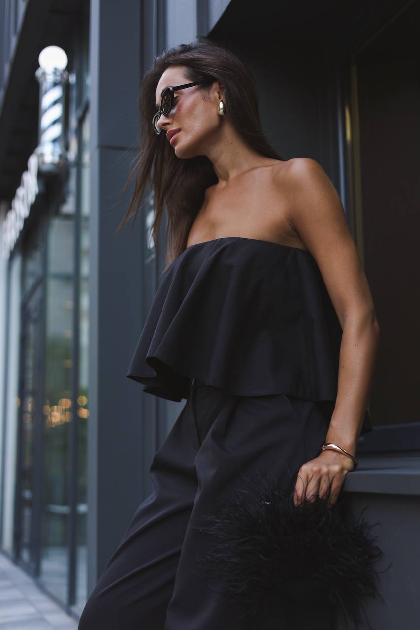 Woman in a black strapless dress standing against a dark building.