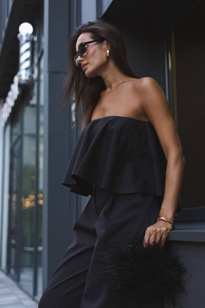 Woman in a black strapless dress standing against a dark building.
