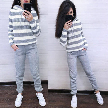 Person wearing a gray and white striped sweater and gray sweatpants, standing against a white wall.