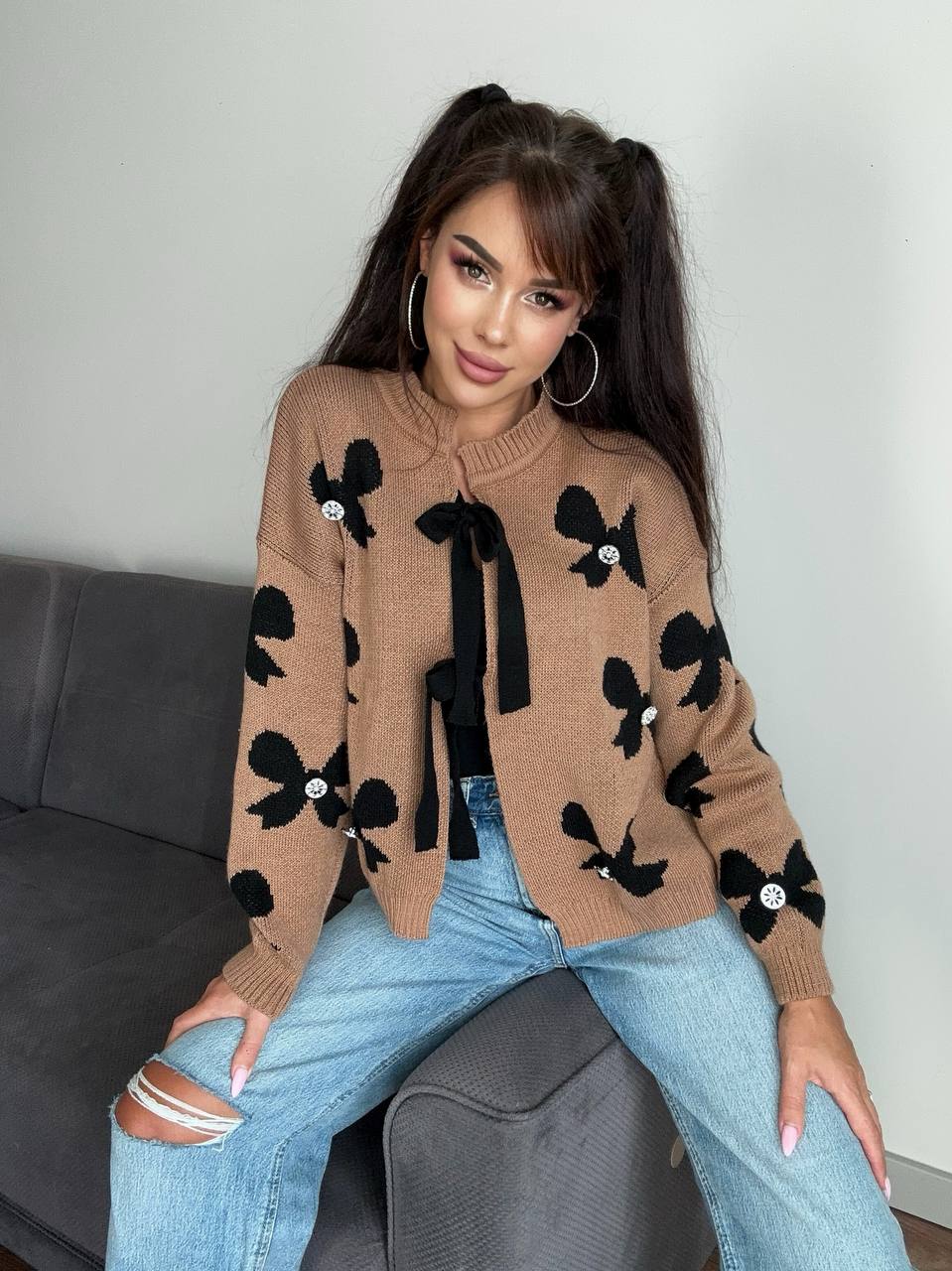 Woman wearing a brown sweater with black bow patterns sitting on a couch.
