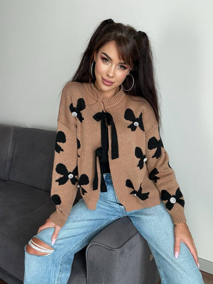 Woman wearing a brown sweater with black bow patterns sitting on a couch.