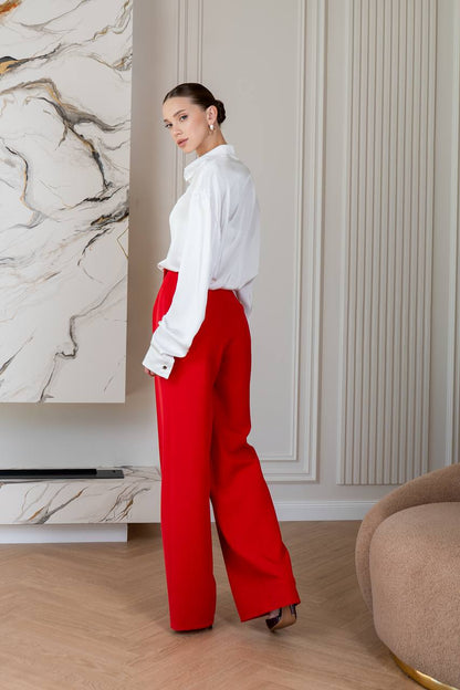 Woman wearing a white blouse and red pants in an indoor setting with marble wall and beige furniture.