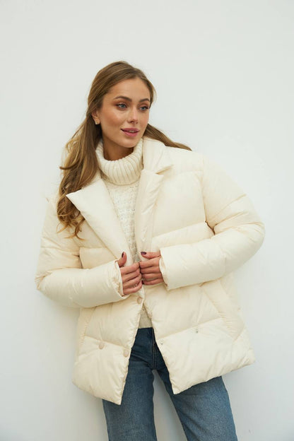 Woman wearing a cream puffer jacket and turtleneck against a white background
