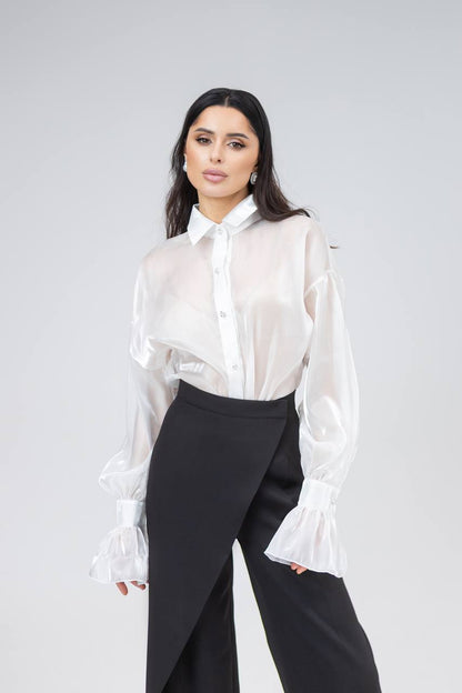 Woman wearing a white blouse and black pants against a gray background