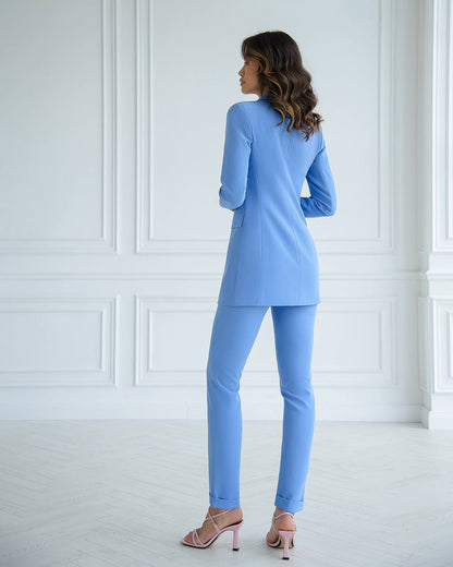 Woman wearing a light blue suit standing in a room with white walls and floor.