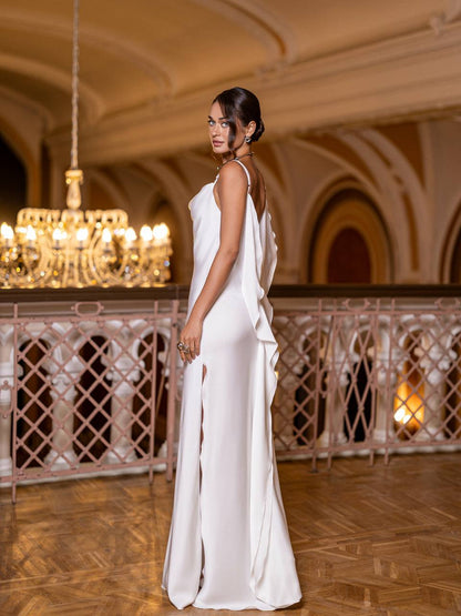 Woman in a white dress standing in an elegant indoor setting with chandeliers.