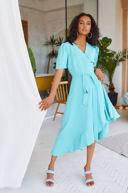 Woman wearing a light blue dress in an indoor setting with plants and furniture.