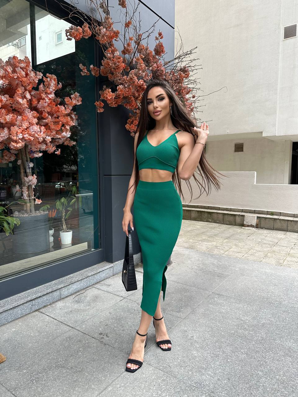 Woman in a green outfit standing on a city street with floral decorations.