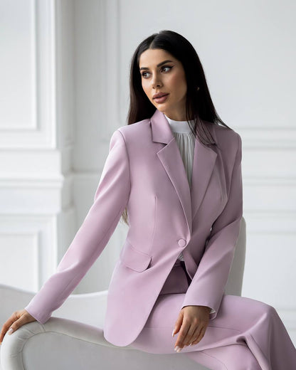 Woman wearing a light pink suit sitting on a white chair against a white wall.