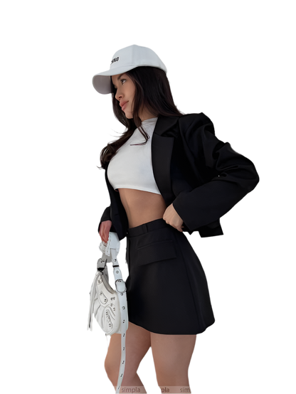 Woman in black blazer and skirt with white top, holding a white bag on a white background