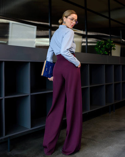 Woman in a light blue shirt and purple pants standing in an office setting.