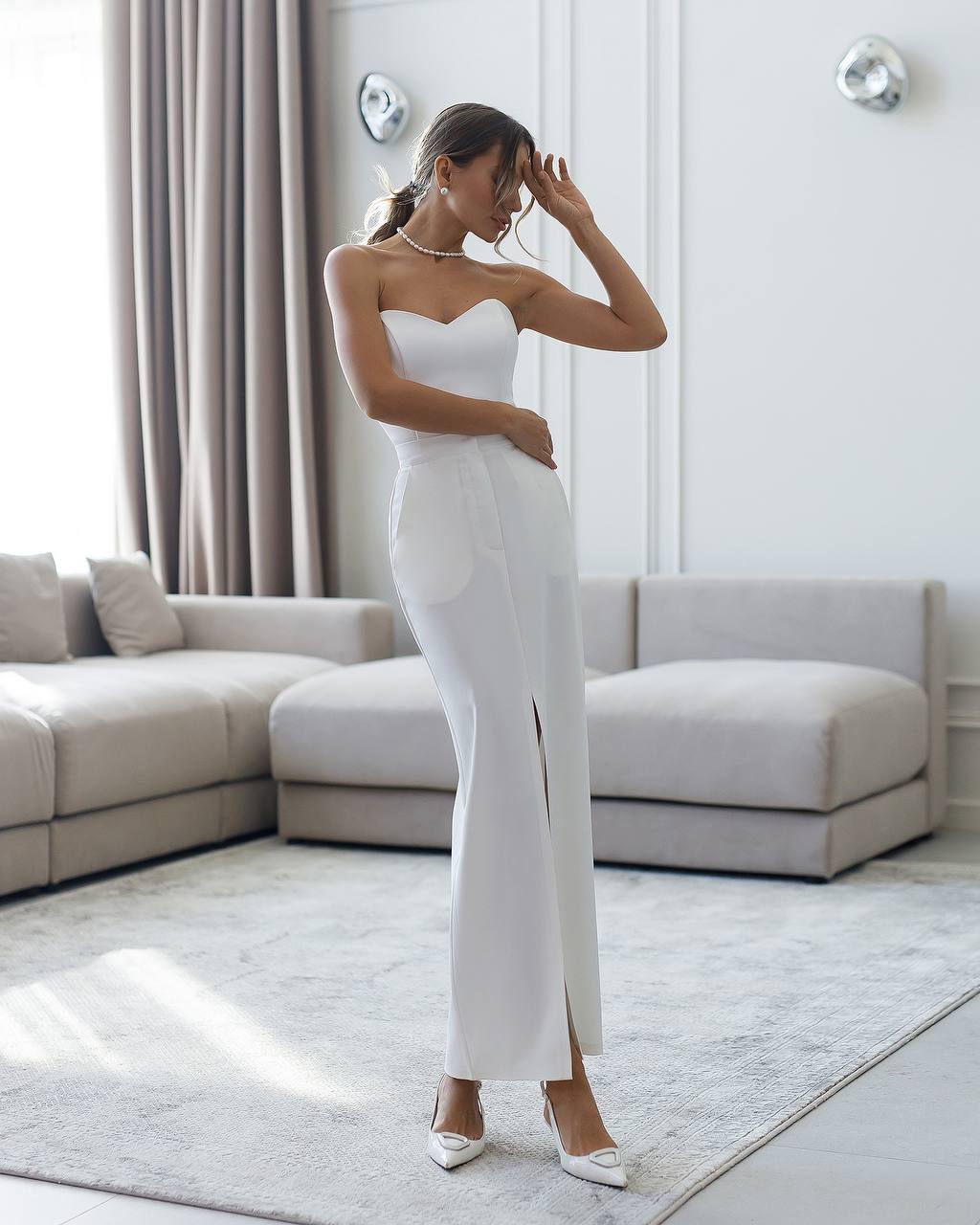 Woman in a white strapless gown standing in a modern living room.