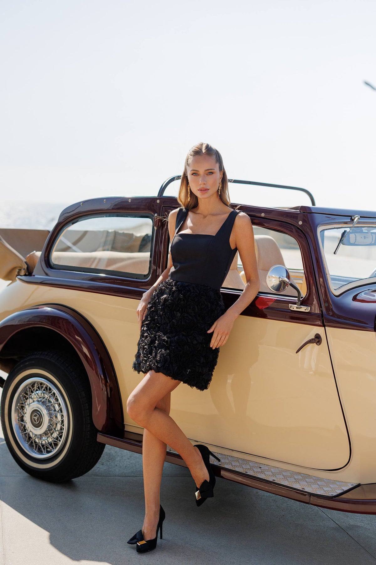 Woman in a black dress standing next to a vintage car