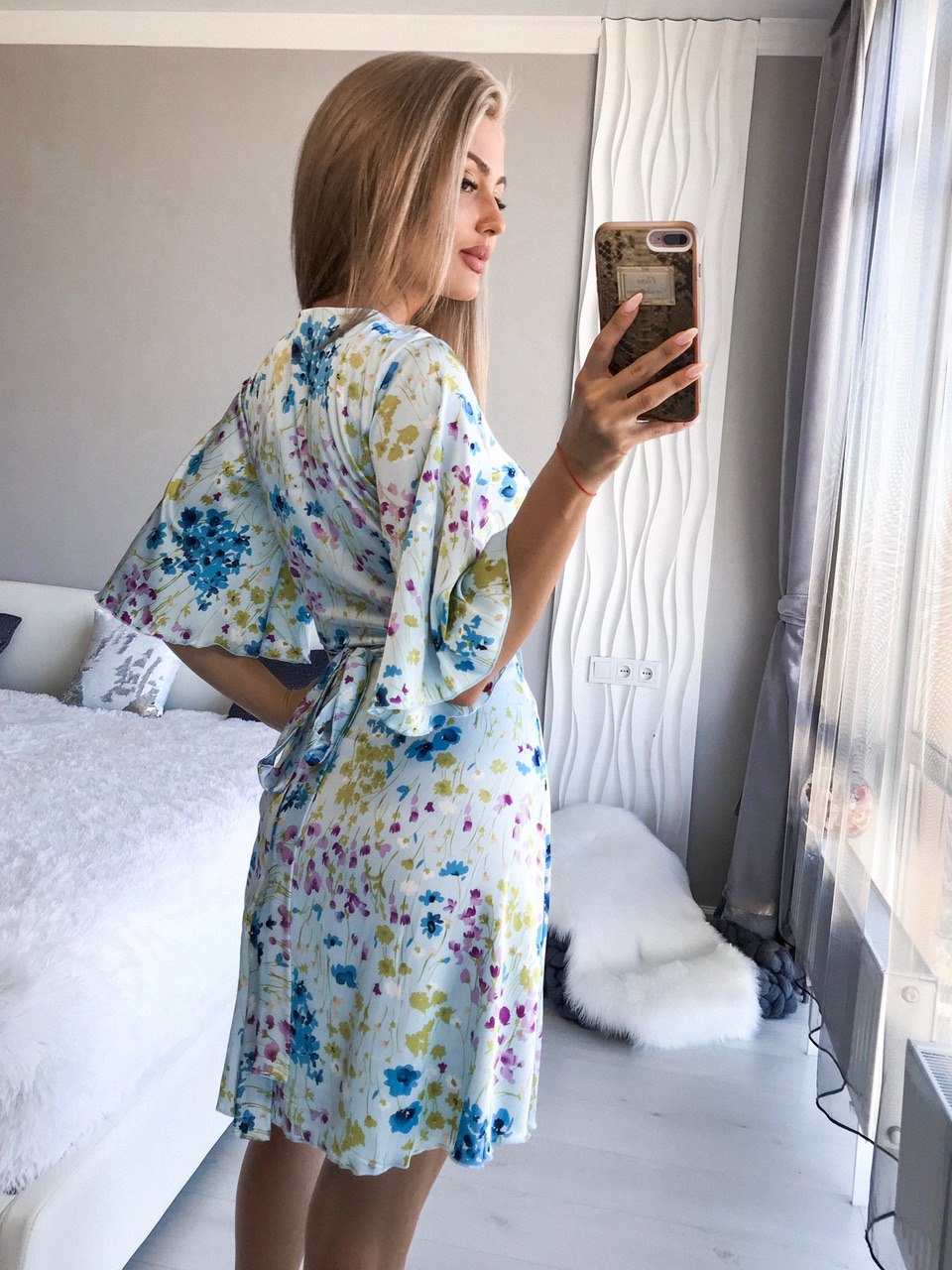 Woman taking a mirror selfie wearing a floral robe in a bedroom.