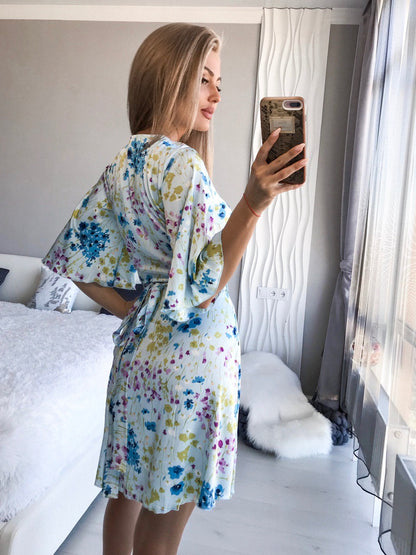 Woman taking a mirror selfie wearing a floral robe in a bedroom.