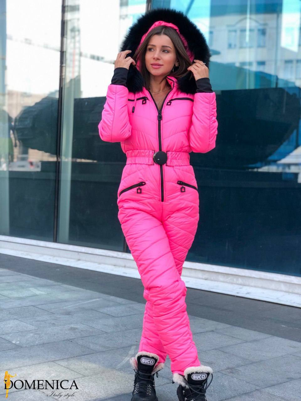 Person wearing a pink puffer suit with a fur-lined hood in an urban setting.