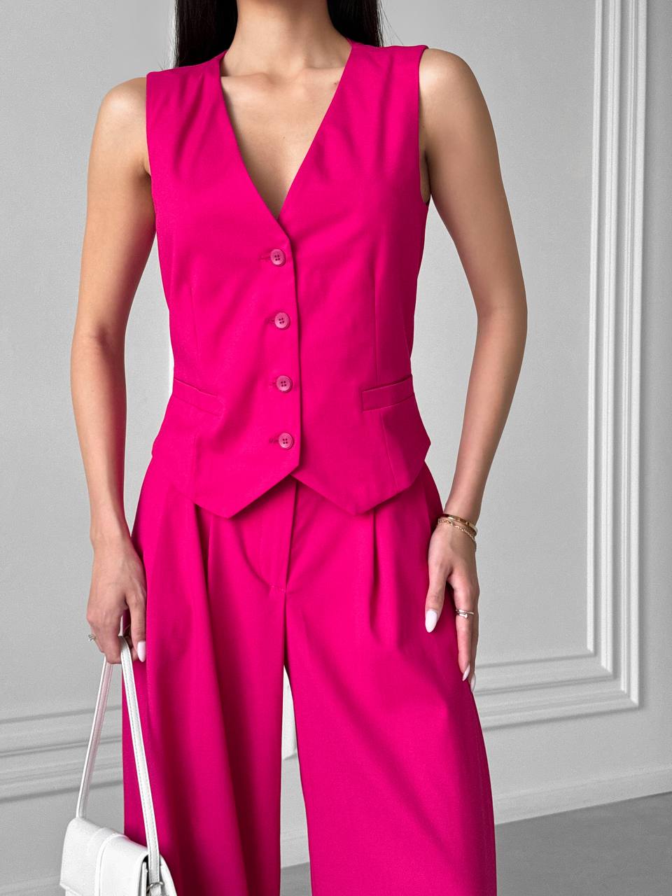 Person wearing a bright pink sleeveless jumpsuit with a plain background