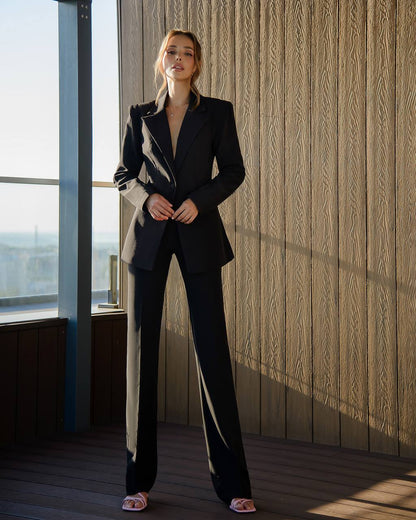 Woman in a black and white suit standing in a room with wooden paneling and a window.
