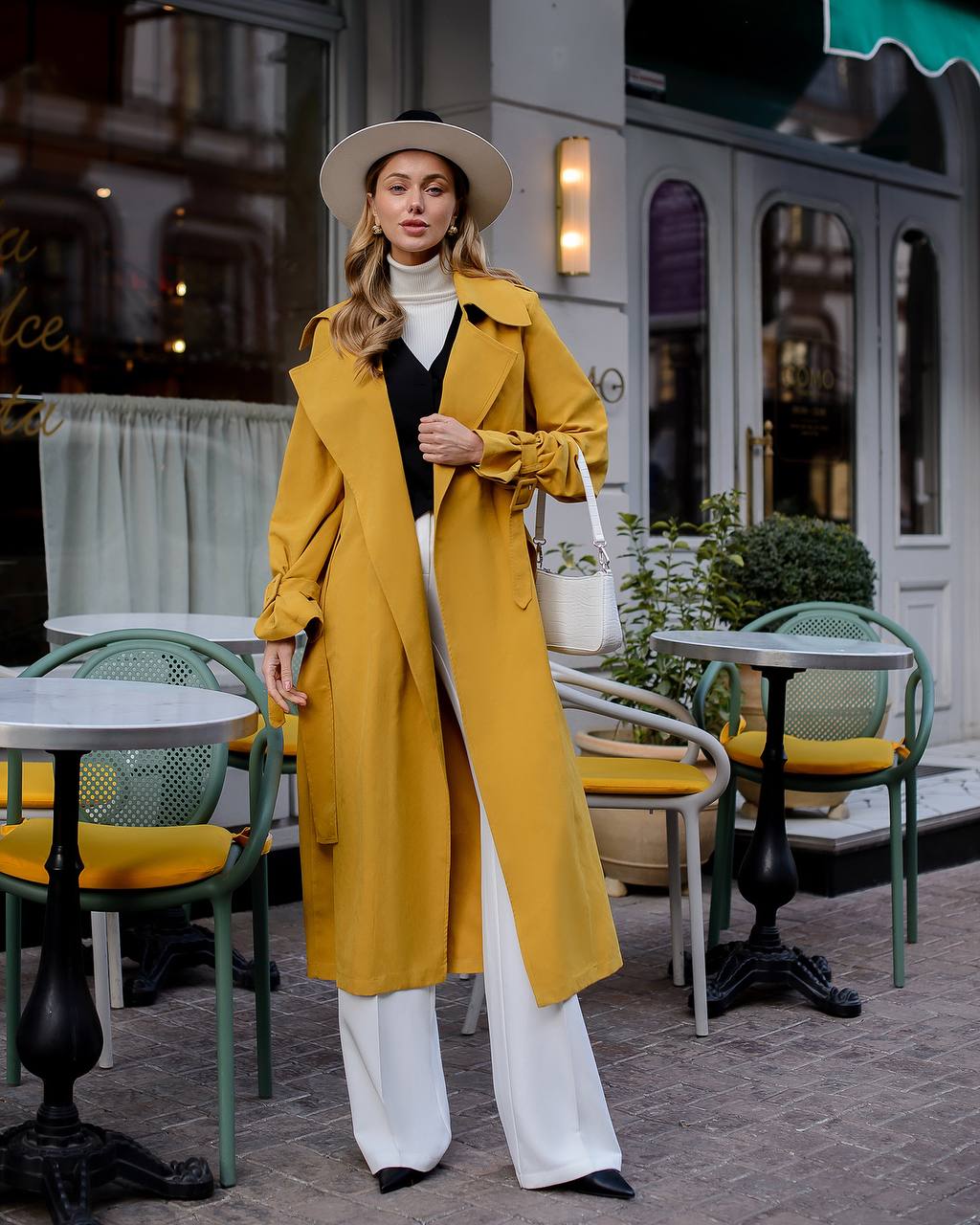 Woman in a yellow trench coat standing in an outdoor cafe setting