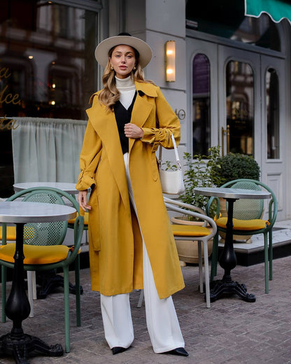 Woman in a yellow trench coat standing in an outdoor cafe setting