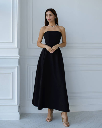 Woman wearing a black strapless dress against a white wall