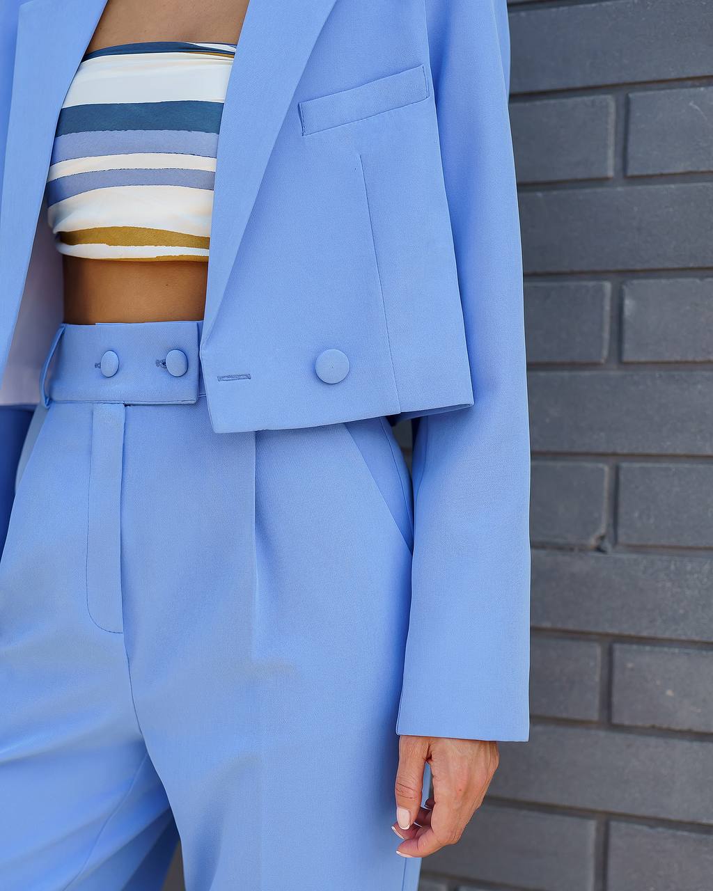 Person wearing a light blue suit with a striped top against a gray brick wall.