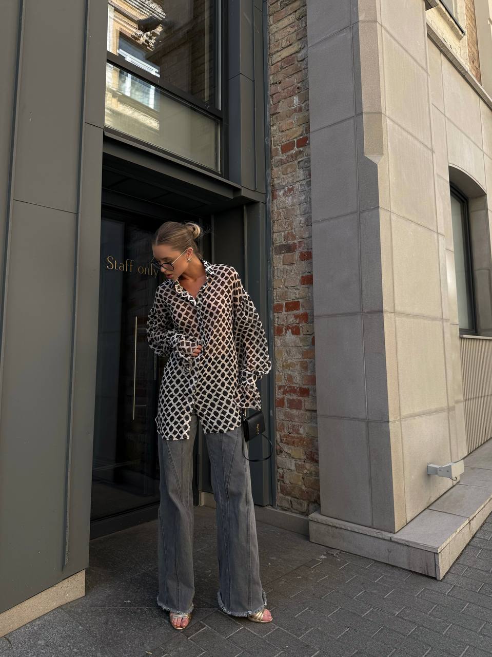 Woman walking out of a building wearing a patterned blouse and jeans.