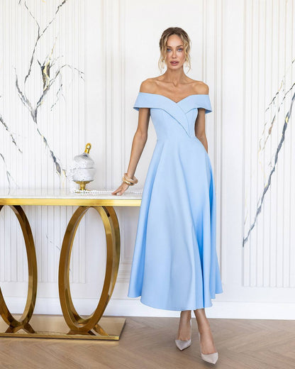 Woman in a light blue off-shoulder dress standing in a stylish room with a gold table and marble wall.