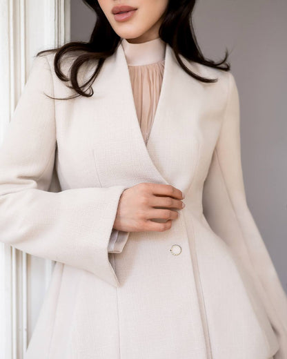 Close-up of a person wearing a light-colored coat with a neutral background