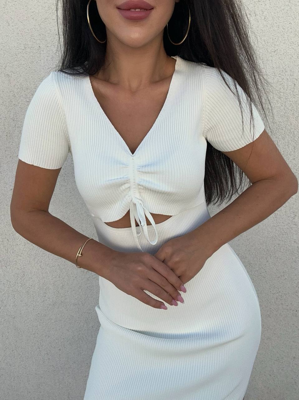 Woman wearing a white ribbed top with cut-out design against a neutral background