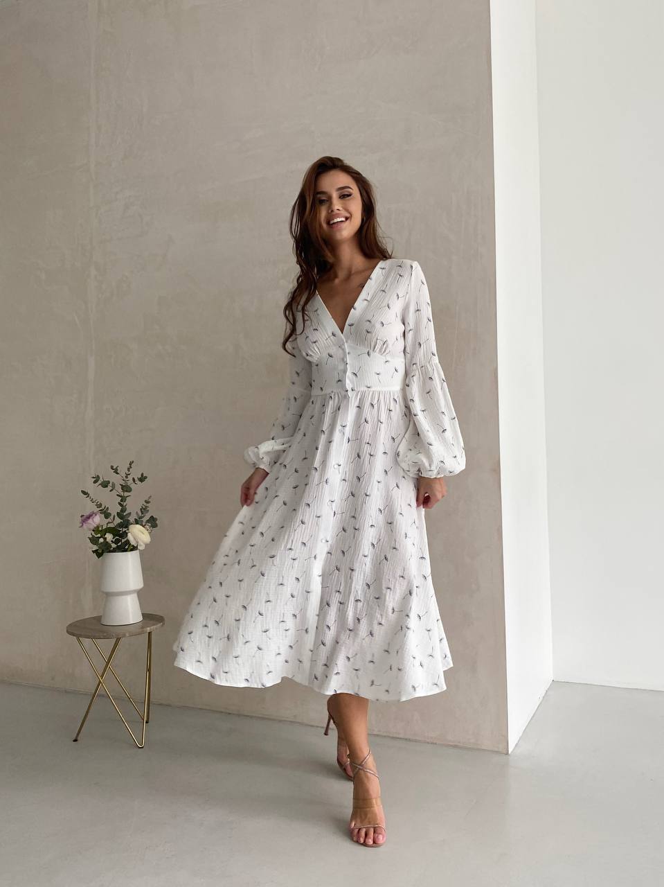 Woman wearing a white dress with a subtle pattern, standing in a minimalistic room.