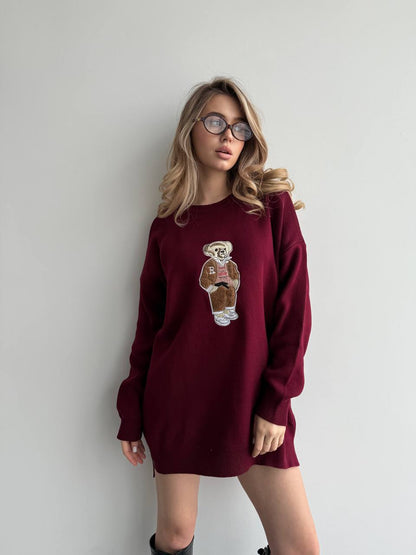 Woman wearing a burgundy sweater dress with a teddy bear design against a plain background